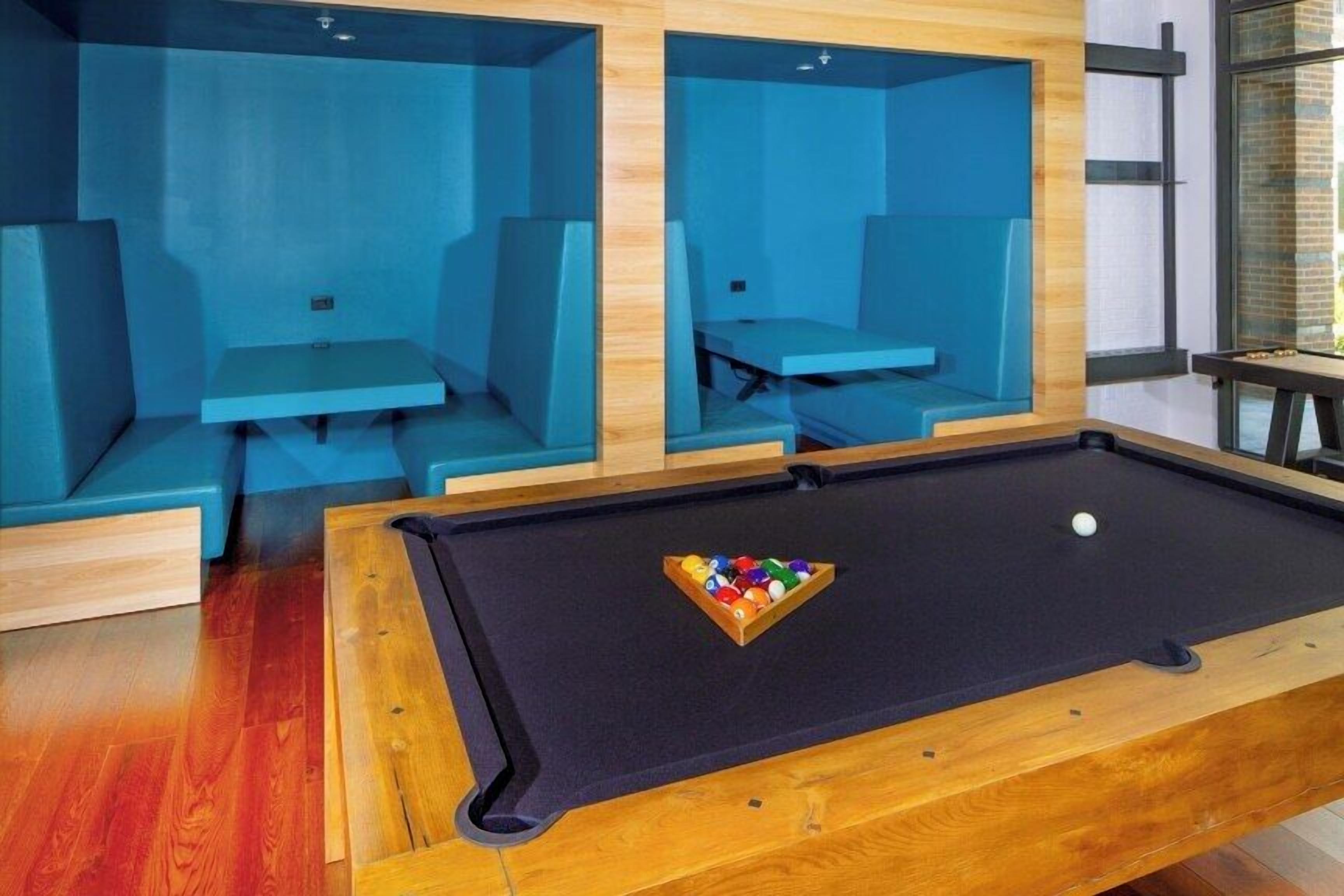 Une table de billard avec un porte-billes et des coins salon dotés de coussins bleus.
