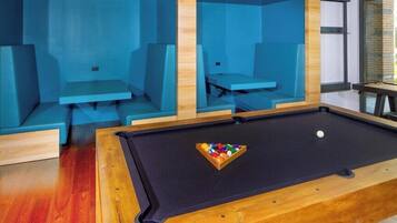 Une table de billard avec un porte-billes et des coins salon dotés de coussins bleus.