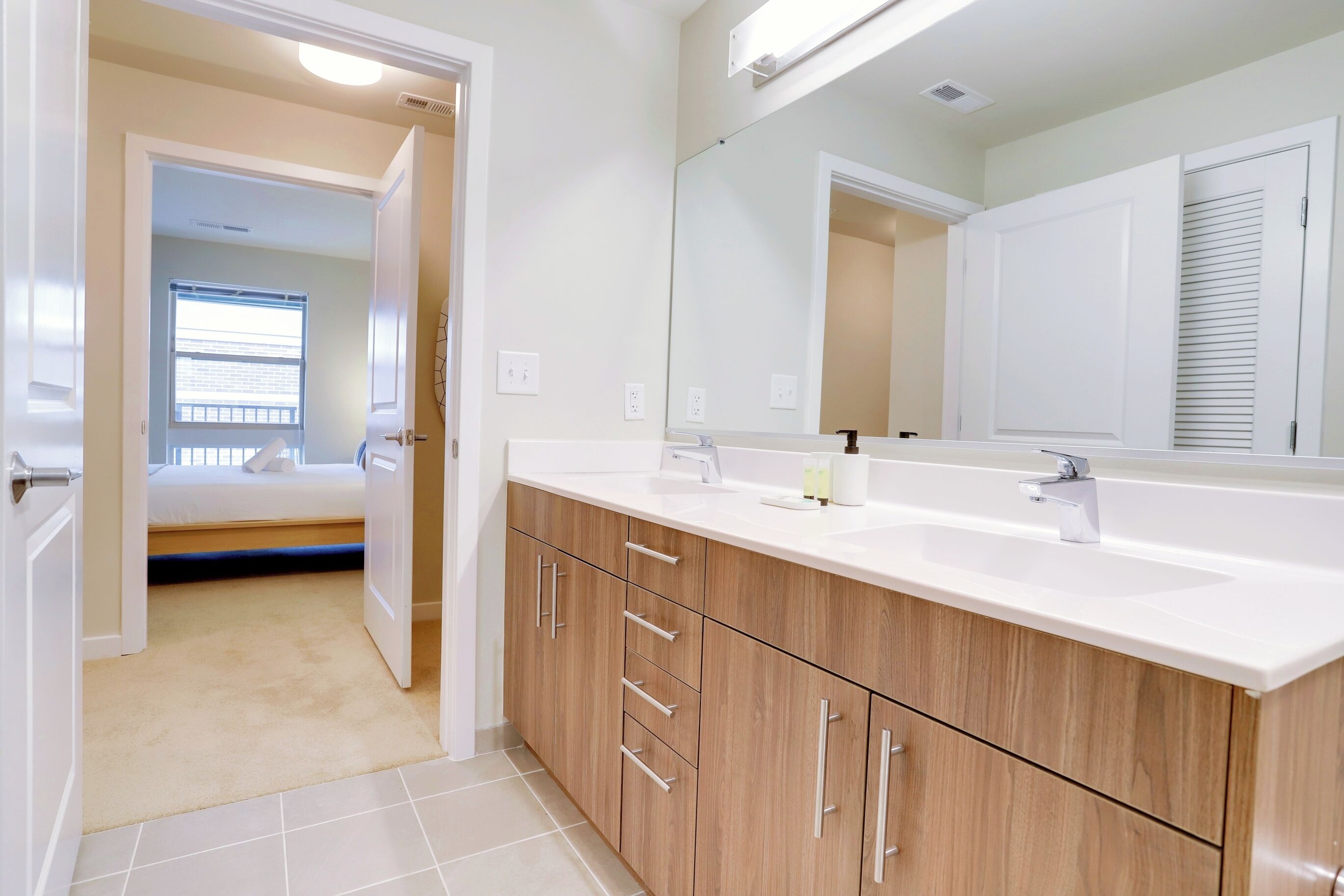 A modern bathroom with a large mirror, wooden cabinets, and a white countertop.