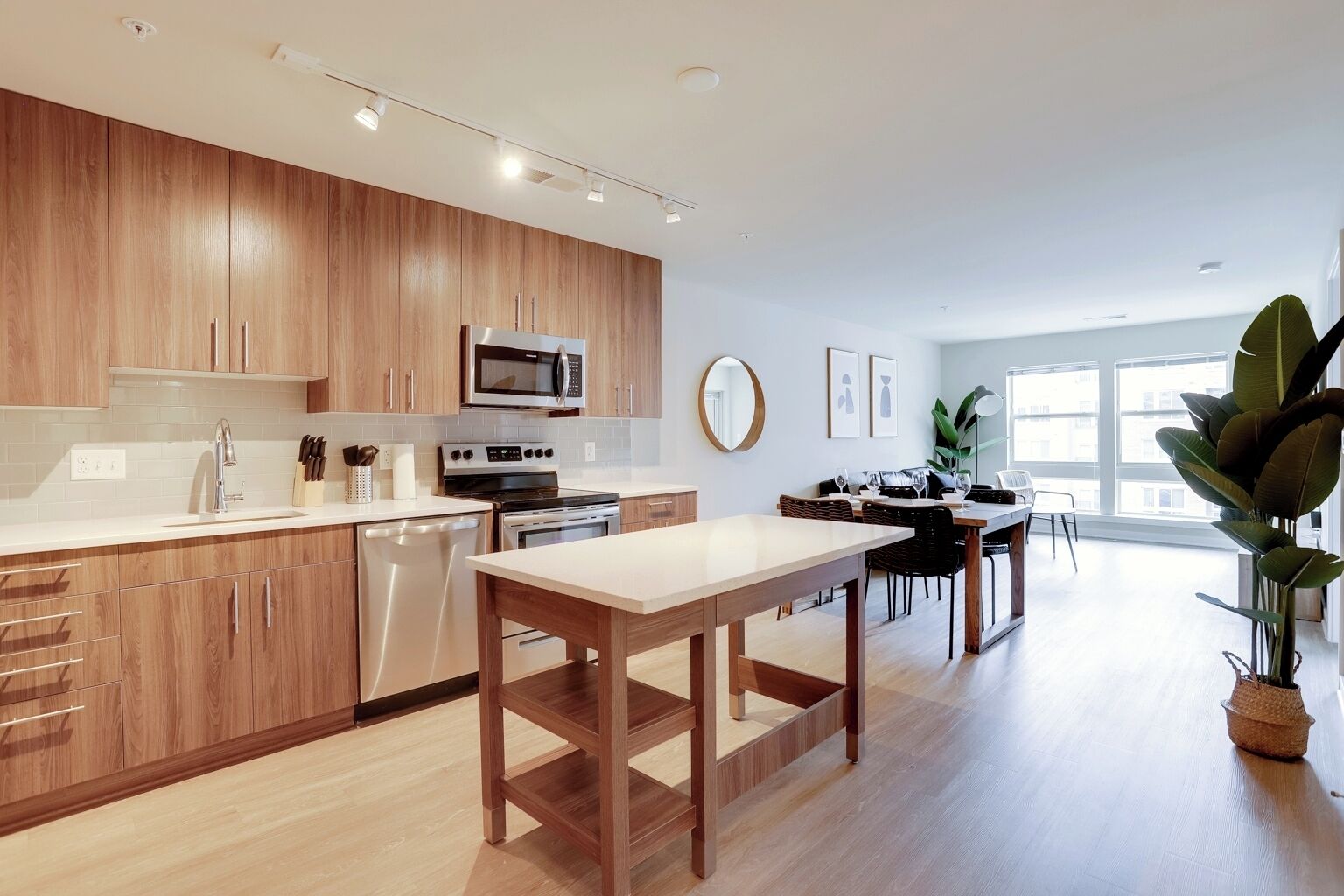 A modern kitchen with wooden cabinets, stainless steel appliances, and a dining area with a large window.
