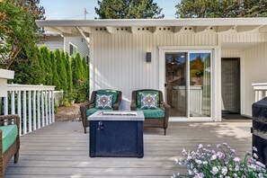 A covered outdoor seating area with two wicker chairs, a table with a water dispenser, and a glass door leading to a covered porch.