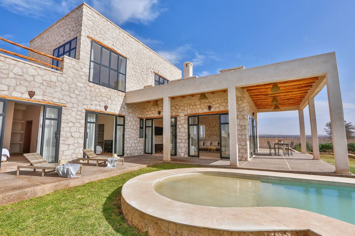 A modern house with a stone facade, a swimming pool, and outdoor seating areas.
