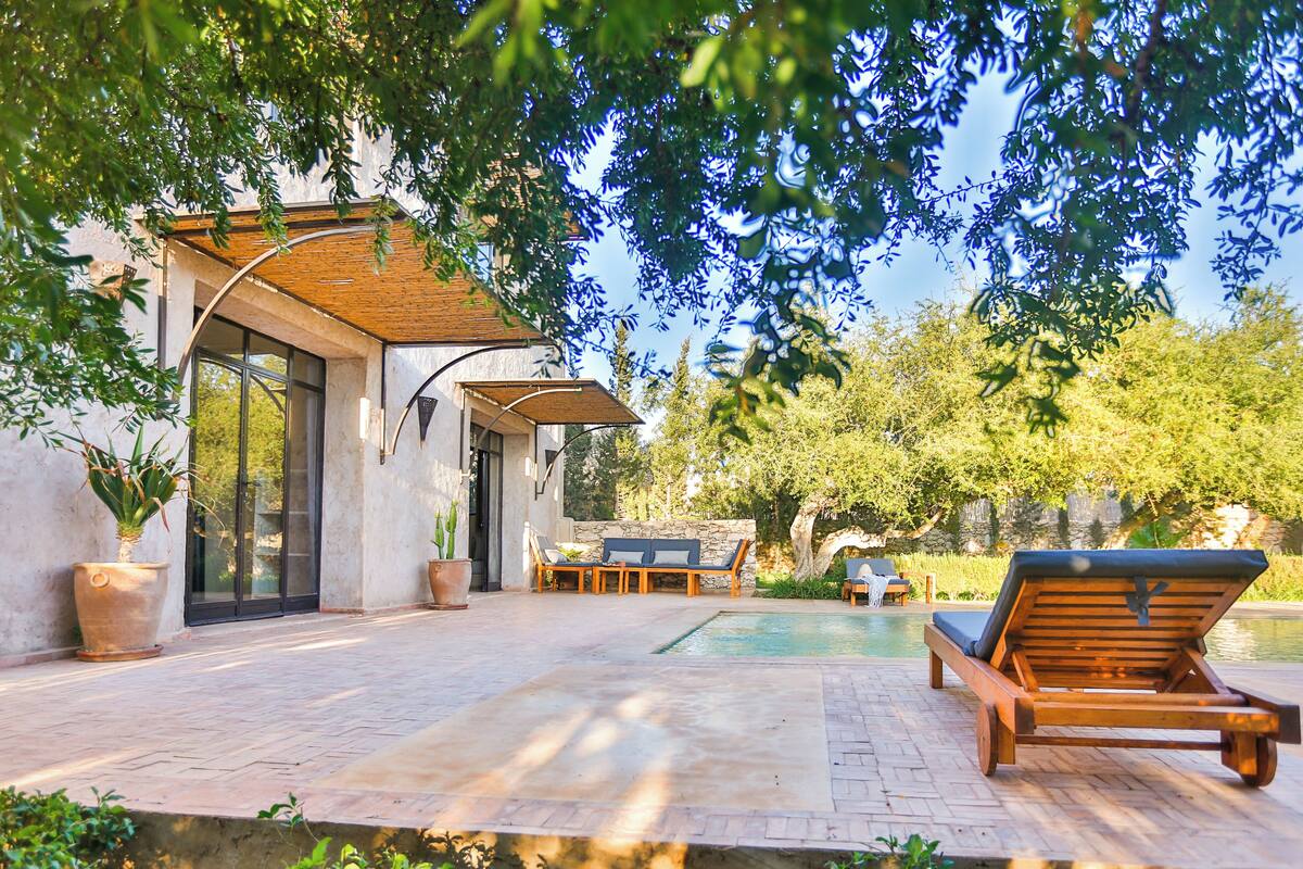 A modern outdoor patio with a swimming pool, lounge chairs, and a stone wall.