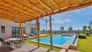 Ein Poolbereich mit Pergola, Sitzgelegenheiten im Freien und Blick auf den Pool.