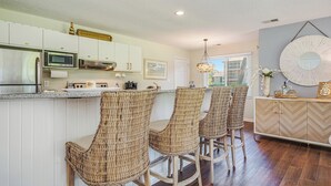 Una cocina moderna con armarios blancos, un refrigerador de acero inoxidable y un microondas integrado. Hay taburetes de mimbre y una mesa de comedor de madera.