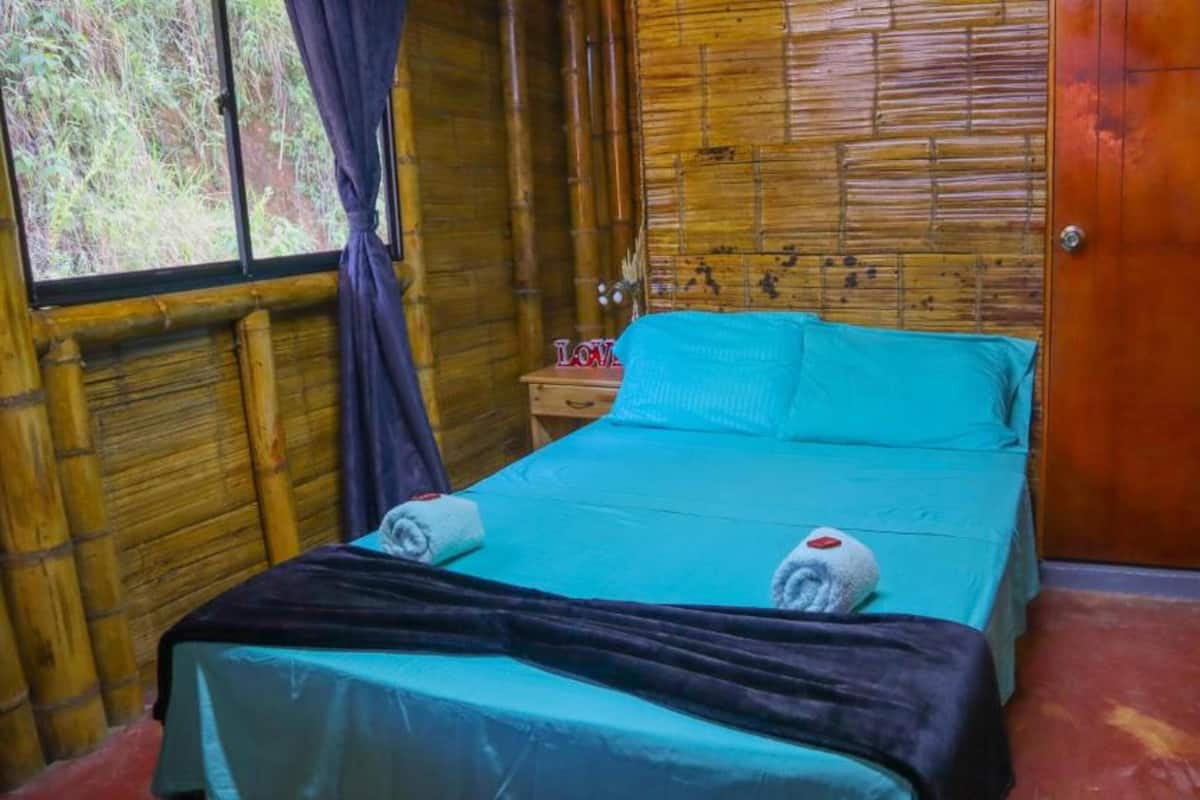 Um quarto com cama, mesa de cabeceira e janela com cortinas.