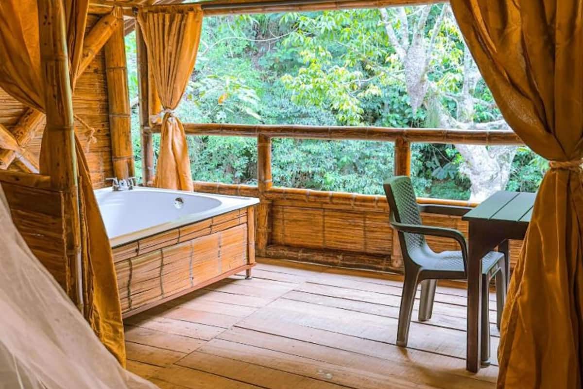 Uma cabana de madeira com uma janela grande, uma banheira e uma mesa com uma cadeira.