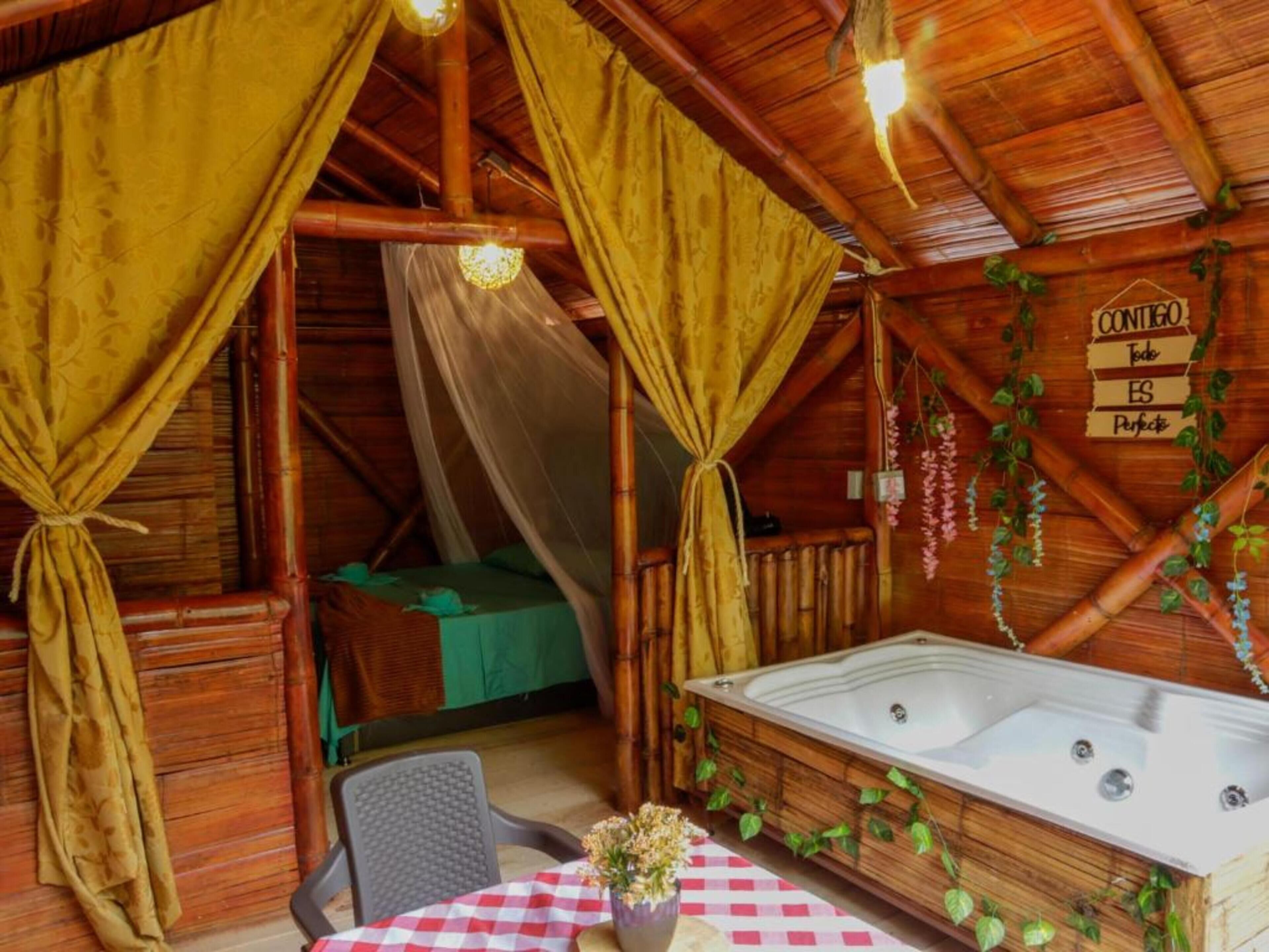 Accogliente baita di legno rustica con un letto, un tavolo con tovaglia a quadretti e una vasca idromassaggio.