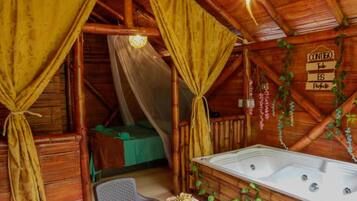 Accogliente baita di legno rustica con un letto, un tavolo con tovaglia a quadretti e una vasca idromassaggio.