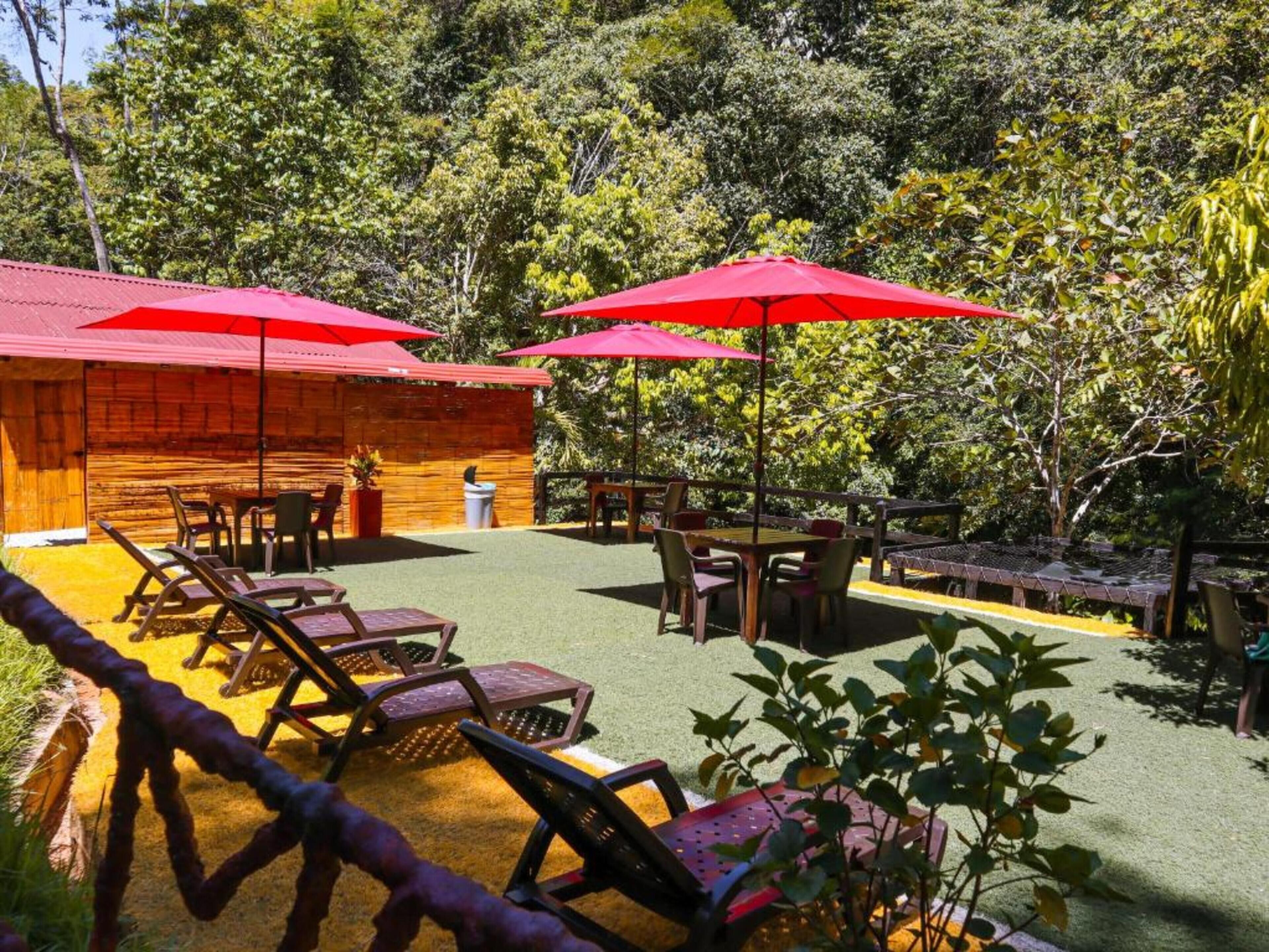 A wooden cabin with a patio area featuring outdoor seating and red umbrellas.