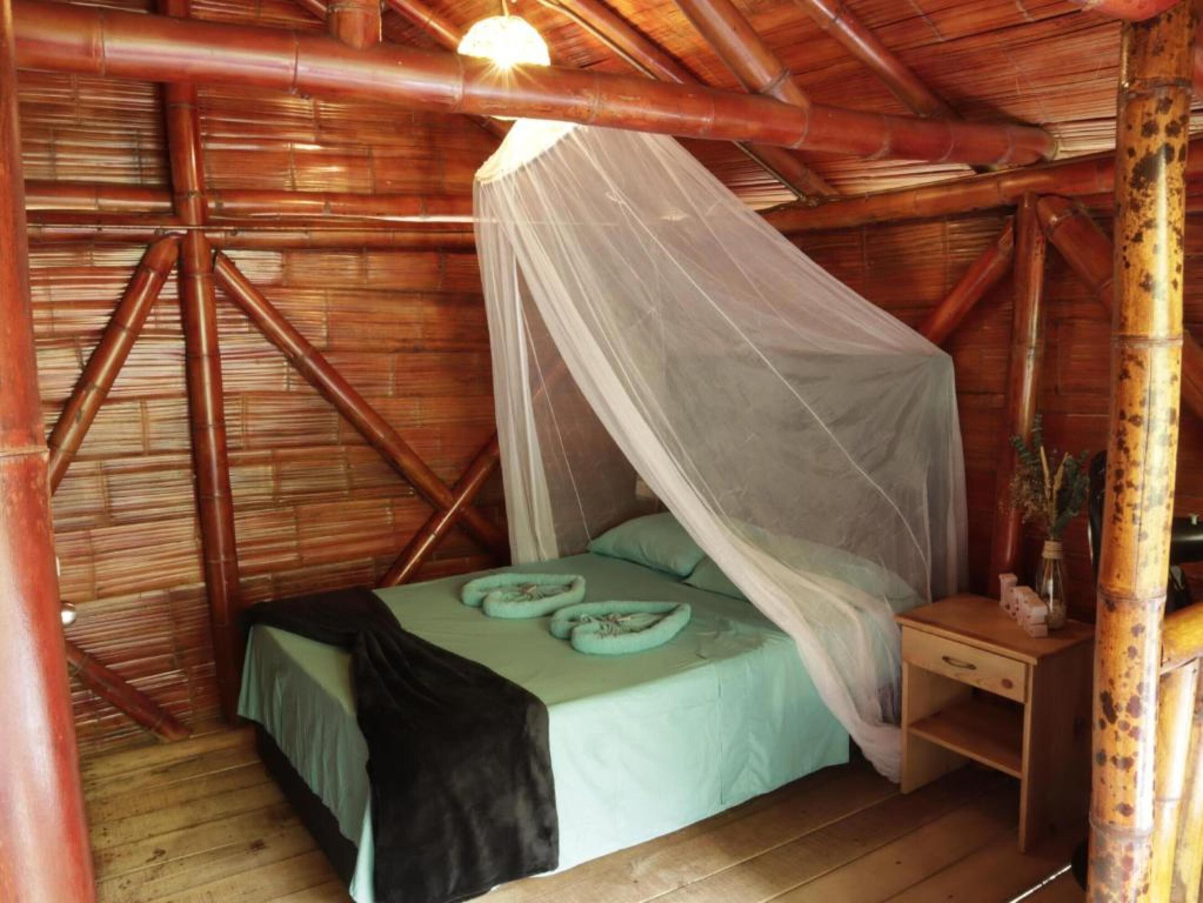 A room with a bed under a canopy, wooden walls, and a nightstand with a lamp.