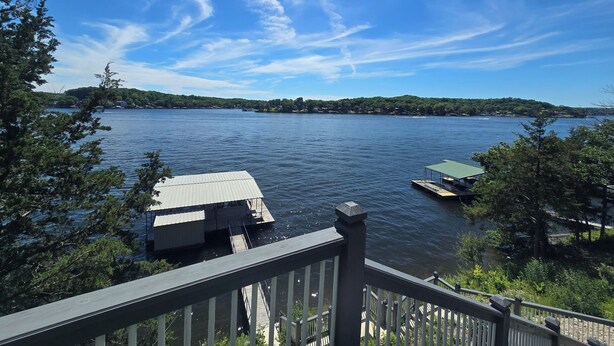 A lakeside view with a dock, a boat, and a house with a green roof. - Ozarks Lake House, Private Dock w/ Boat and Jetski lifts! (Rocky Mount)