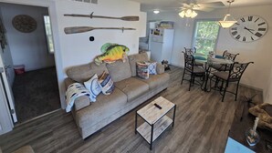A living room with a sofa, coffee table, dining table, chairs, a clock, and a ceiling fan. - Ozarks Lake House, Private Dock w/ Boat and Jetski lifts! (Rocky Mount)