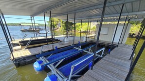 A dock with a covered walkway, a boat, and a small building in the background. - Ozarks Lake House, Private Dock w/ Boat and Jetski lifts! (Rocky Mount)