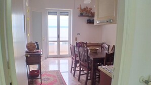 Un couloir mène à une salle à manger où se trouvent une table et des chaises, un tapis et une porte donnant sur l’extérieur.