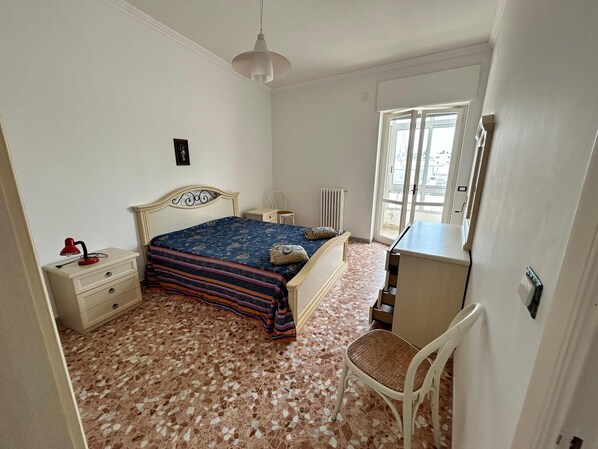 A bedroom with a bed, a desk, a chair, a radiator, and a window.