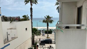 Une vue depuis un balcon donnant sur une plage bordée de palmiers, avec un café et une voiture garée.