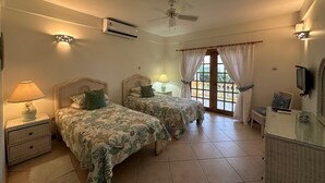 Une chambre d’hôtel avec deux lits, un ventilateur de plafond, un appareil de climatisation, une télévision et un balcon avec des rideaux.