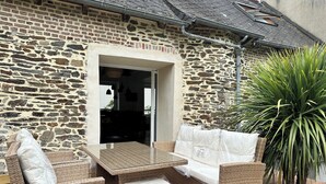A stone building with a patio area featuring wicker furniture and a large plant. - Maison Entièrement Rénovée Avec Billard en Plein Cœur du Légué et à 5 min Plage (Plérin)