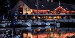 Un bâtiment situé au bord de l’eau, doté d’une structure imposante illuminée de lumière rouge, dont le reflet se mire sur l’eau.