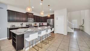A modern kitchen with dark cabinets, a granite countertop, and a central island with bar stools.