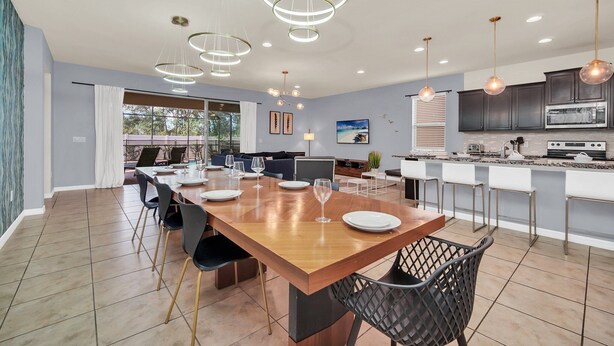 A modern kitchen with dark cabinets, a large island, and a dining area with a wooden table and chairs.