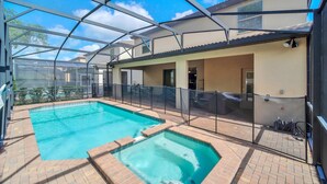 A swimming pool with a glass enclosure, surrounded by a brick patio and a covered area with a metal roof.
