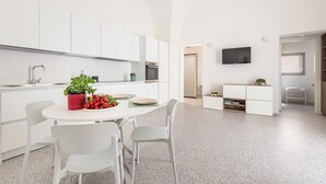 A modern kitchen with white cabinetry, a dining table with chairs, and a television mounted on the wall. - La Piccola Corte - Appartamento1 by BarbarHouse (Maruggio)