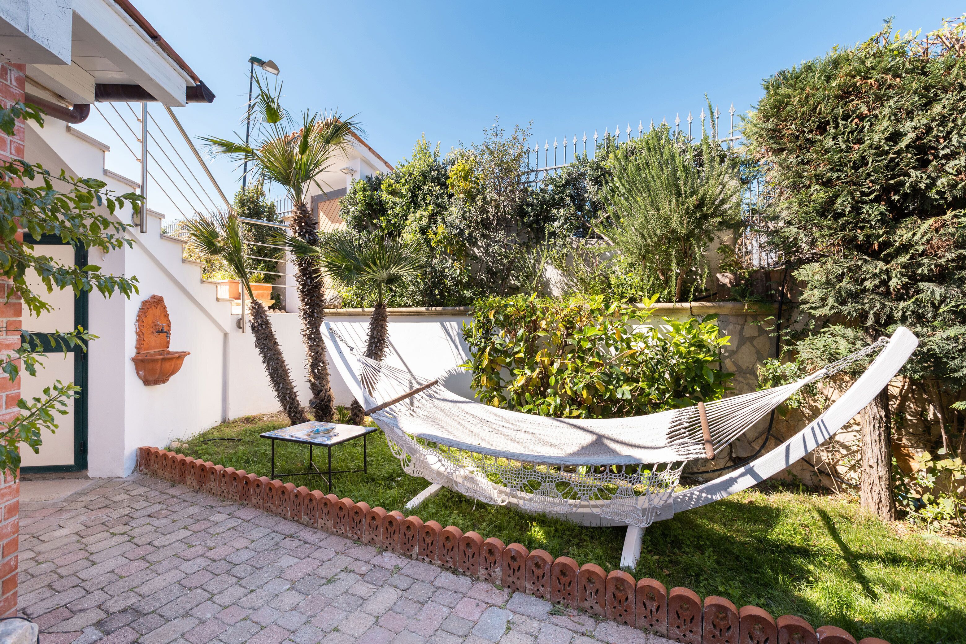 A hammock in a garden with a brick pathway and a white building.