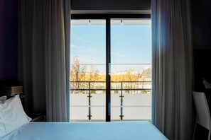 A hotel room with a large bed, a nightstand, a chair, and a view through a glass door to the outside. - Tryp Cordoba Ex Tryp Los Gallos (Córdoba)