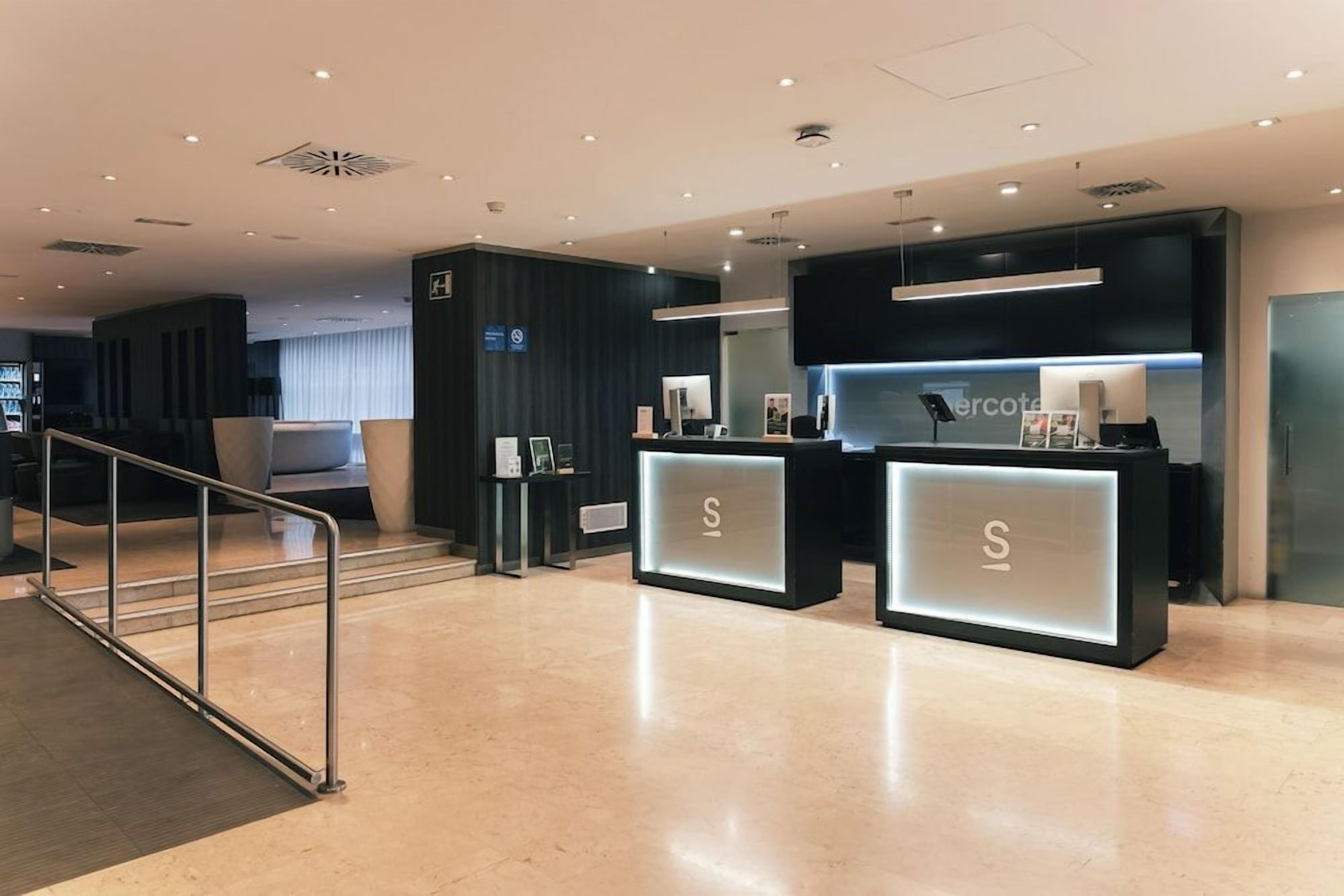 Un moderno vestíbulo de hotel con dos mostradores de recepción, una escalera y una zona de estar.