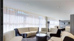 A modern living room with a curved sofa, a coffee table, and a floor lamp. - Tryp Cordoba Ex Tryp Los Gallos (Córdoba)