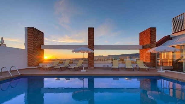 A pool area with lounge chairs and umbrellas, a clear view of the sunset, and a modern architectural design. - Tryp Cordoba Ex Tryp Los Gallos (Córdoba)
