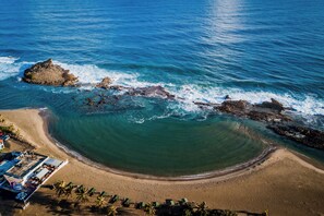 An aerial view of a beach with clear blue water, a sandy shore, and a rocky outcrop. - Oceanfront Oasis SOLAR POWERED beachfront w/ spectacular ocean view (Arecibo)