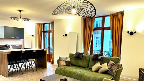 A modern living room with a green sofa, a coffee table, and a dining area with a kitchen counter and chairs. - Spacious apartment in the heart of Gerardmer (Gérardmer)