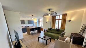 A modern living room with a green sofa, a white armchair, and a coffee table. There is a dining area with a table and chairs in the background. - Spacious apartment in the heart of Gerardmer (Gérardmer)
