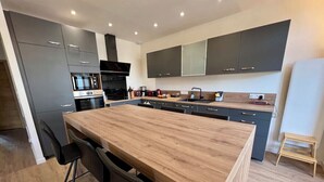 A modern kitchen with dark cabinets, a wooden island, and a built-in oven. - Spacious apartment in the heart of Gerardmer (Gérardmer)