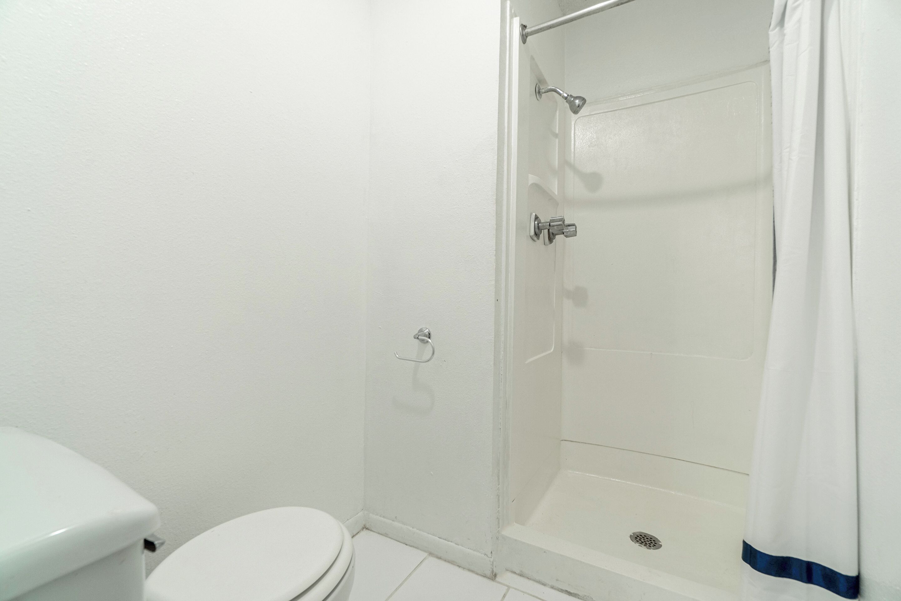 A bathroom with a toilet, a shower with a glass door, and a white shower curtain.