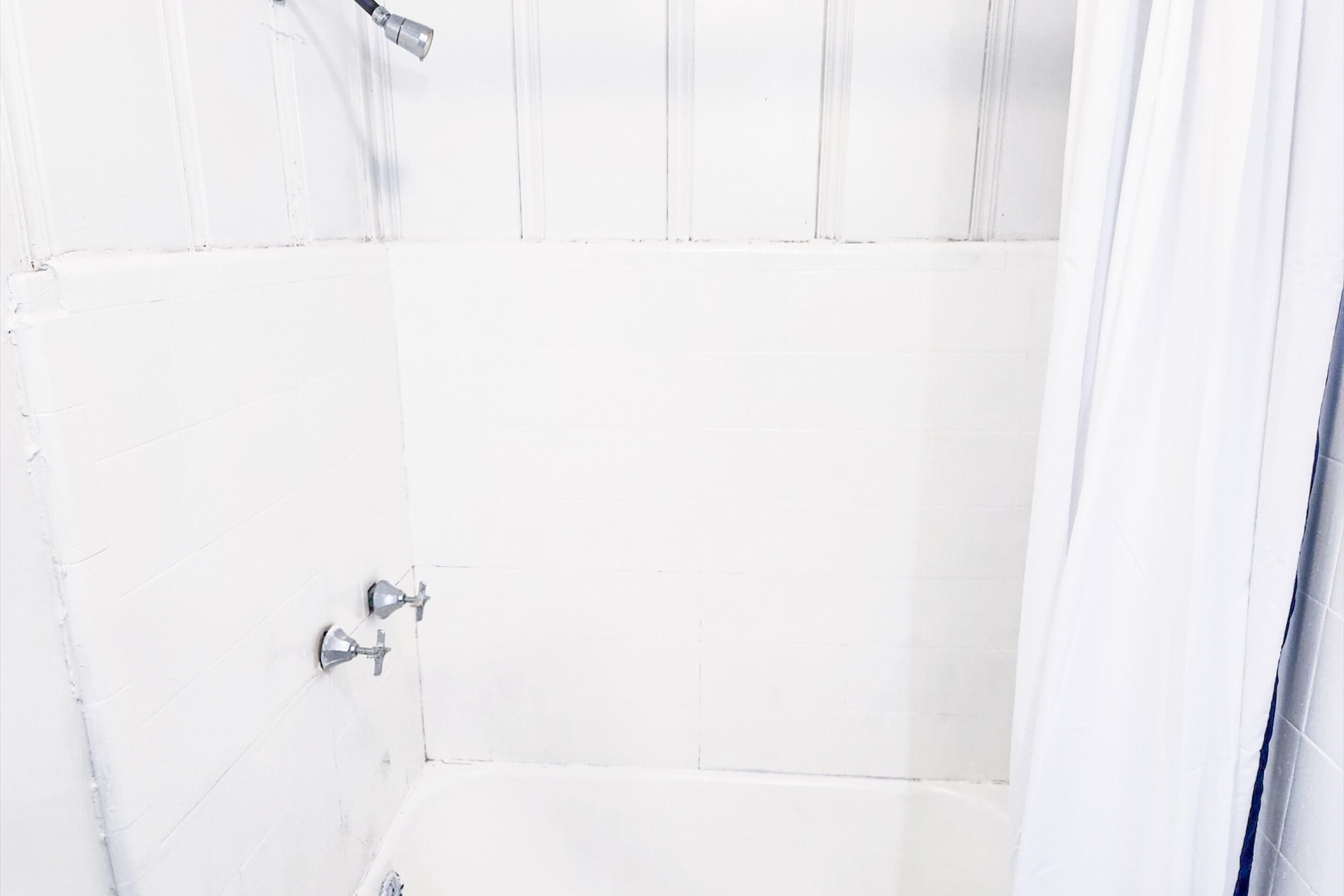 A white tiled shower with a showerhead and a faucet.