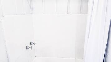 A white tiled shower with a showerhead and a faucet.