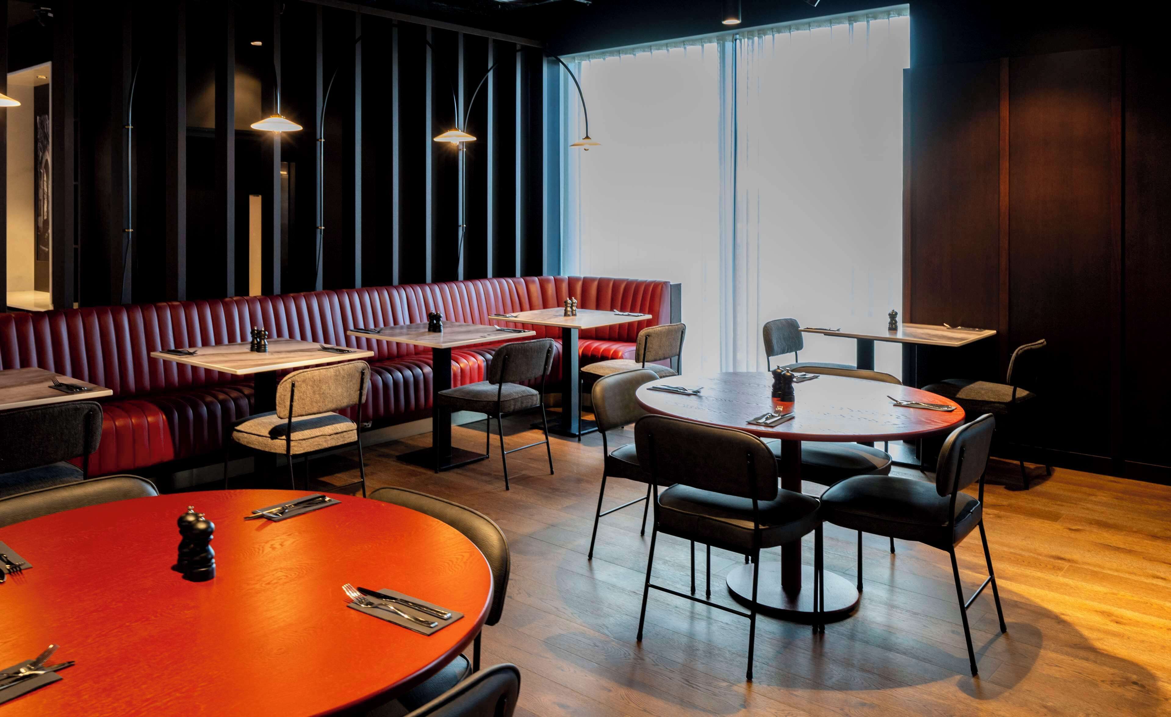 A restaurant with round tables, booths, and a high ceiling.