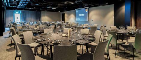 A conference room with multiple tables set for dining, equipped with chairs, plates, cutlery, and glasses.