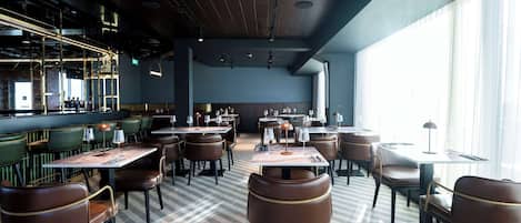 Un restaurante con piso a cuadros, asientos tapizados en verde y una zona de bar con barandilla metálica.