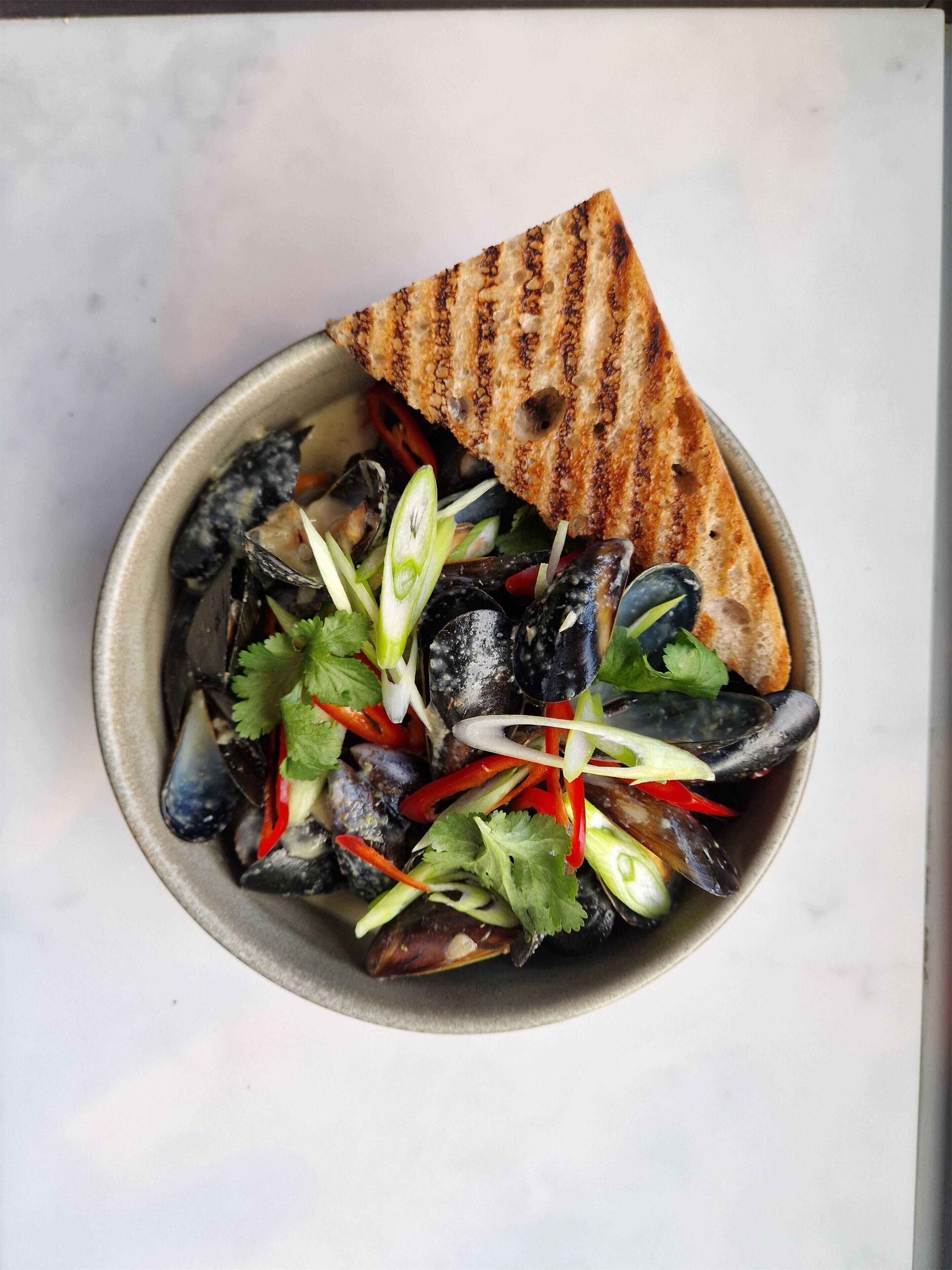 Un plato de mejillones a la parrilla con vegetales y una rebanada de pan tostado.