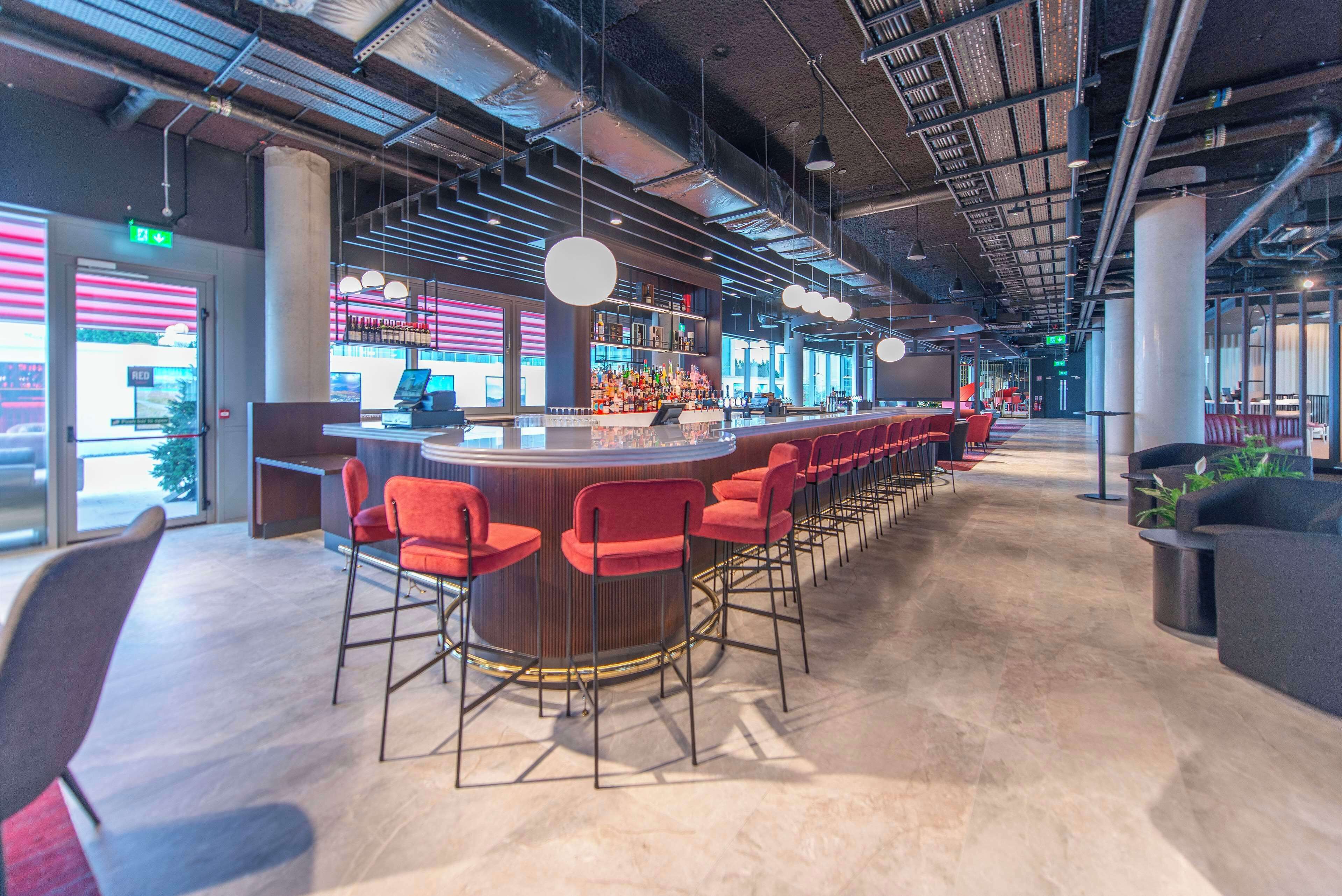 A modern bar area with a long counter, red bar stools, and pendant lighting.