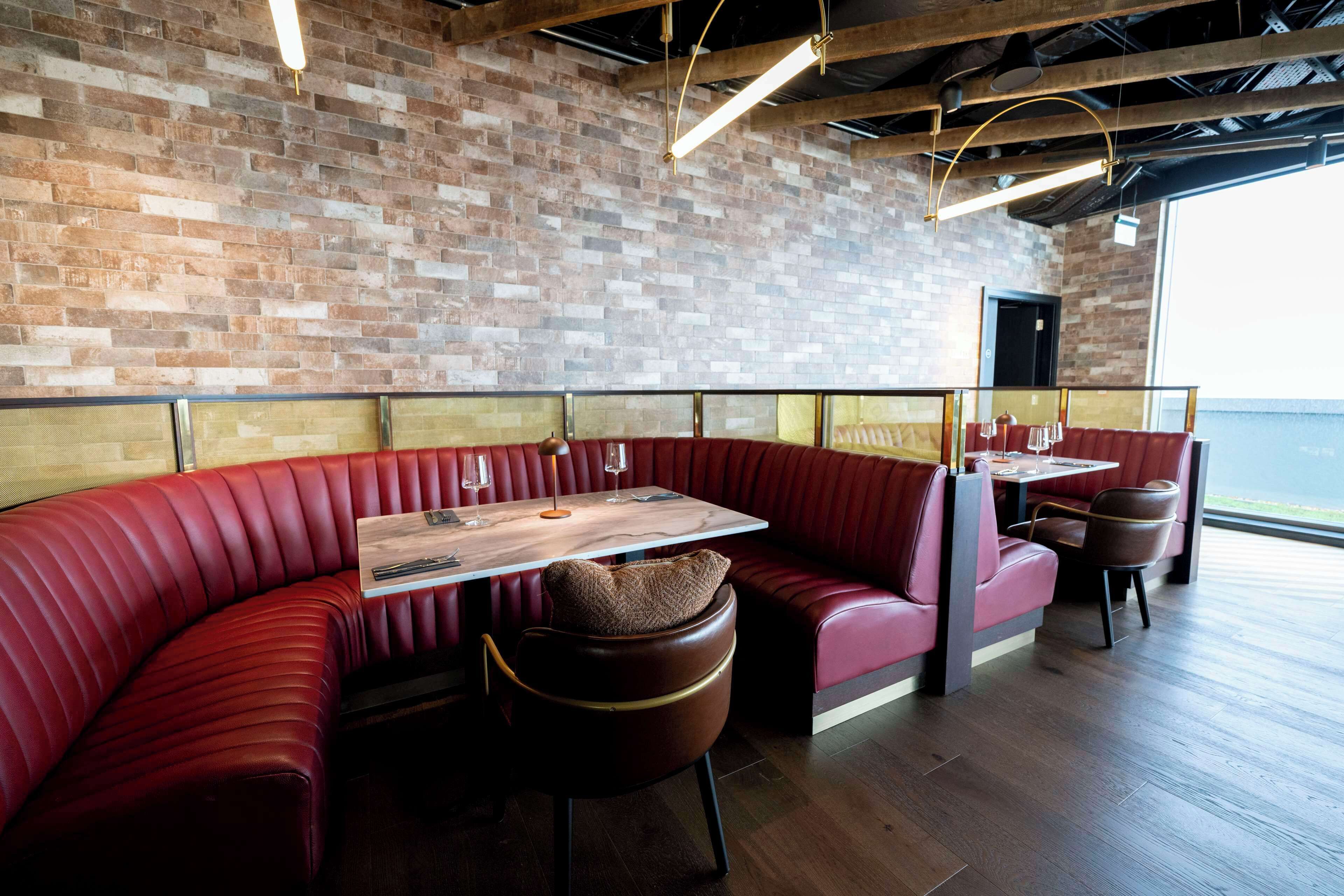 Un restaurante con pared de ladrillo, asientos rojos y una mesa de madera.