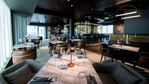 A modern restaurant with a bar area, seating arrangements, and a view of the cityscape. - Radisson RED Galway (Galway)