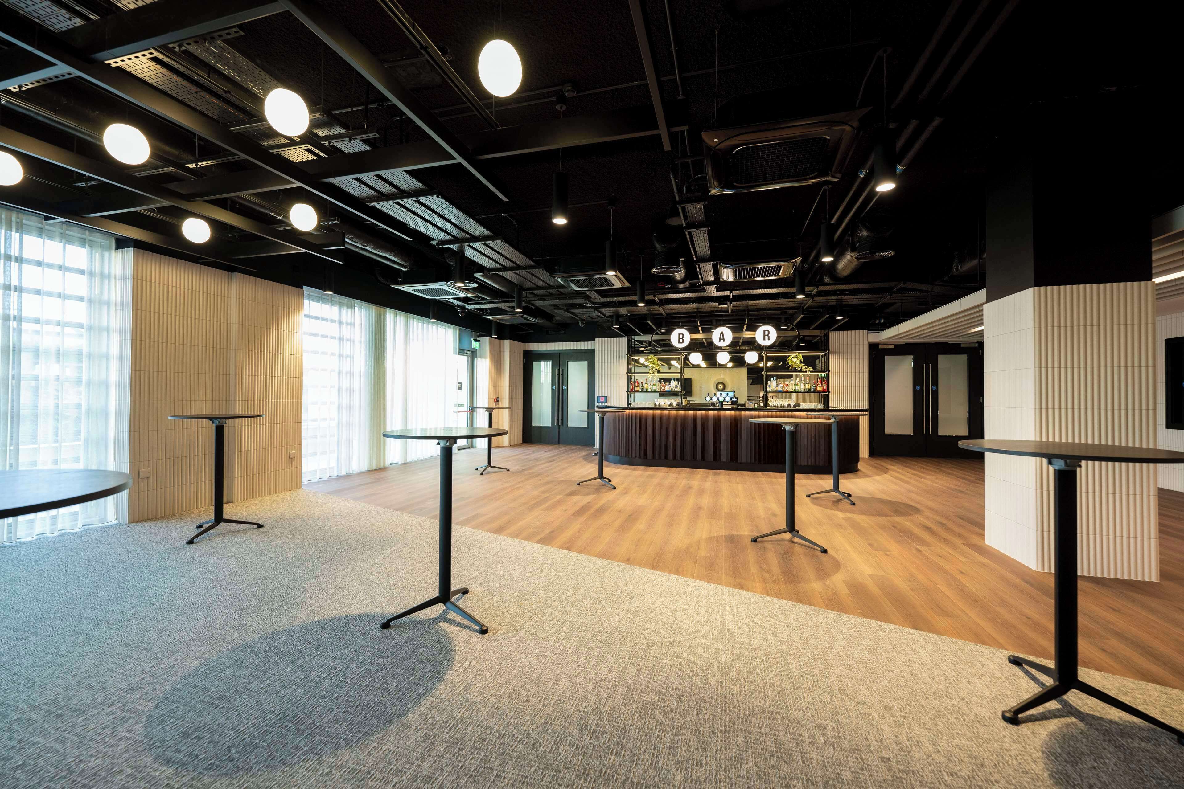 A modern conference room with a bar area, carpeted flooring, and large windows allowing natural light.