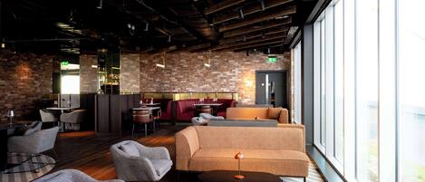 A modern interior with a brick wall, a sofa, chairs, a table, and a bar area.