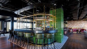 A bar area with a curved counter, multiple stools, and a green partition. - Radisson RED Galway (Galway)
